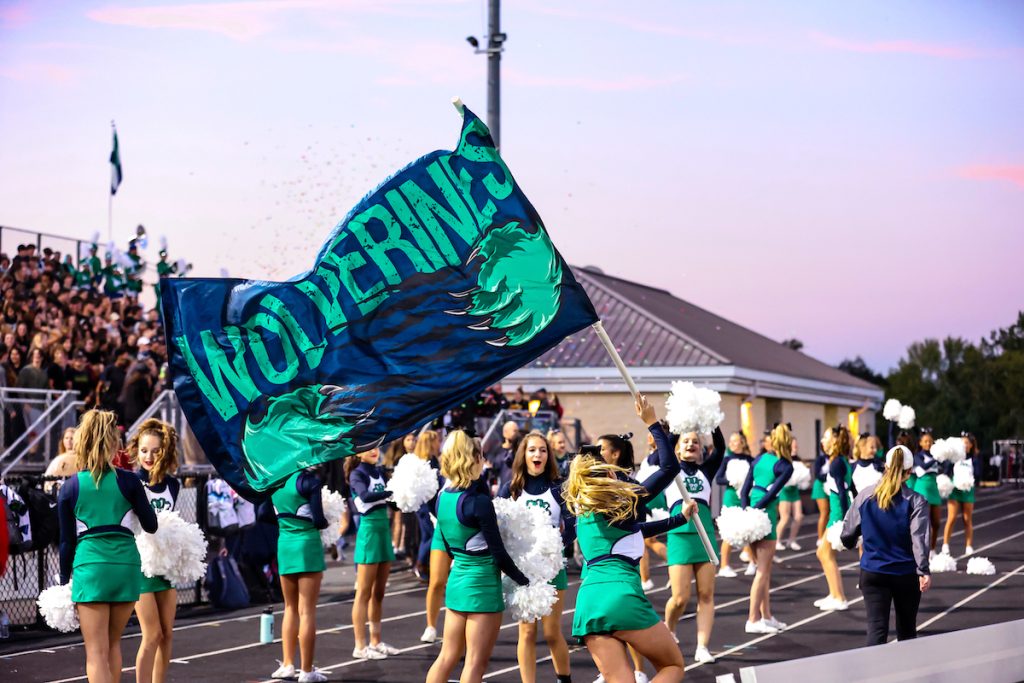 Woodgrove High School cheerleaders holding Wolverines field runner flag in front of crowd at stadium